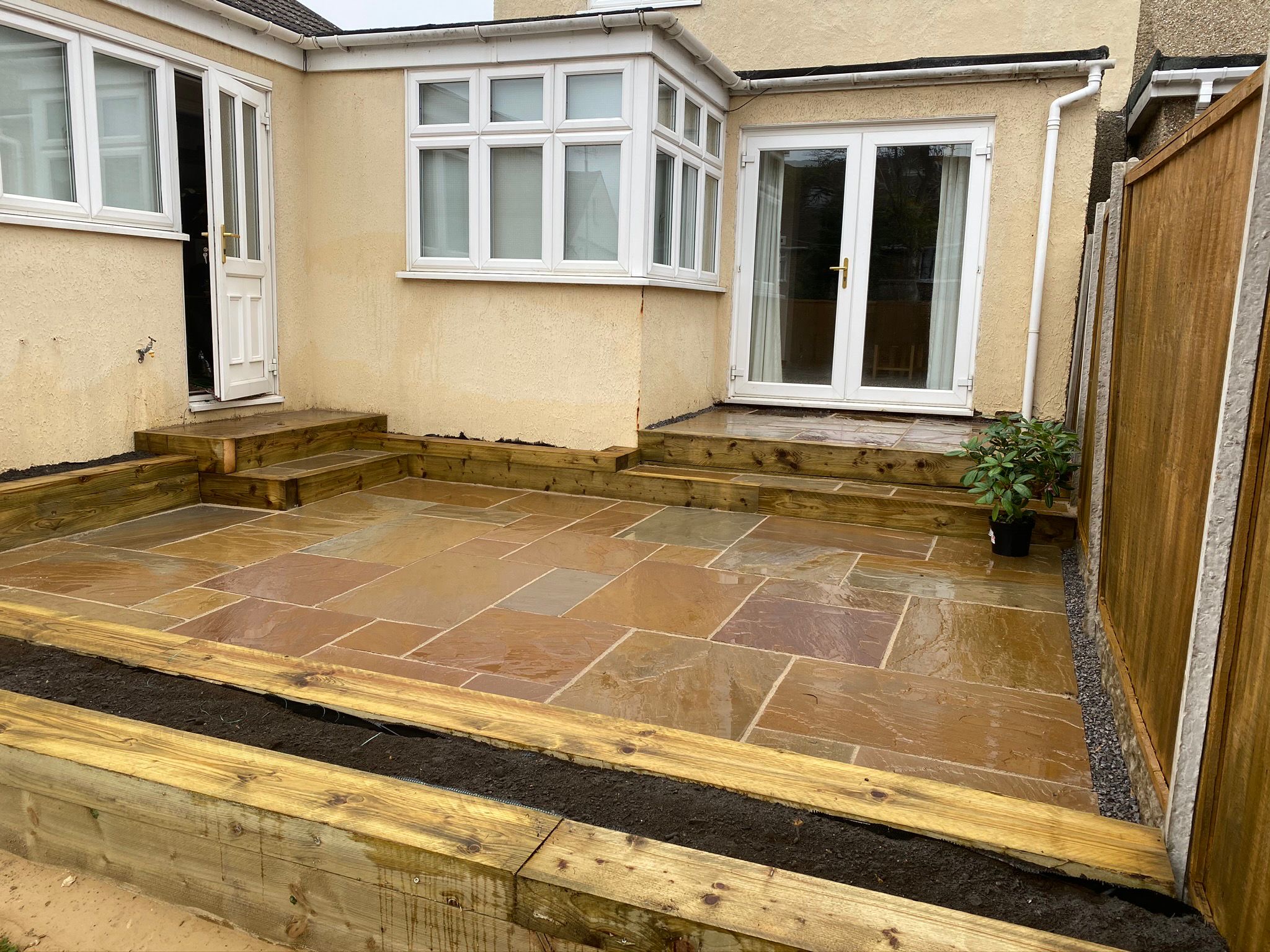Natural stone patio with timber retaining beds by the house